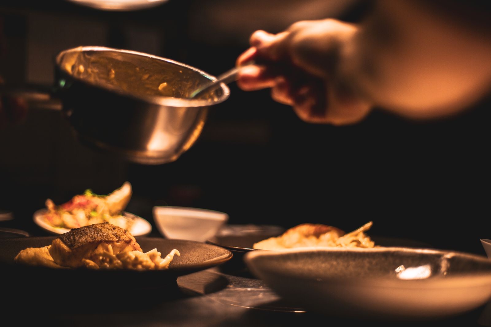 Finished dishes being plated and sauced in a restaurant kitchen